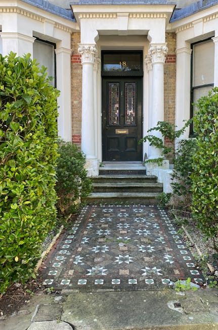 The image depicts the entrance to a historic terraced house with a black front door set in a white-painted classical portico featuring decorative columns and intricate moulding details. The doorway is